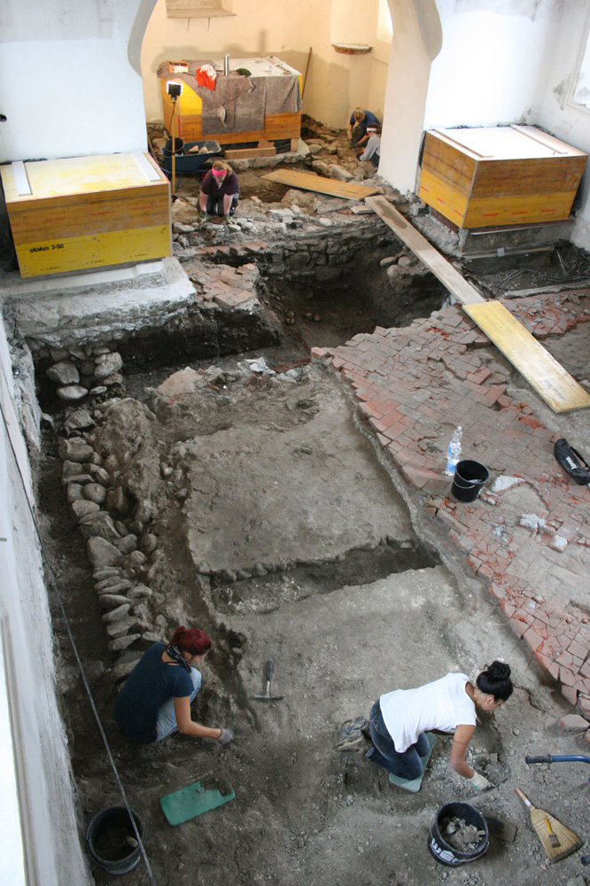 Freilegungsarbeiten im Chor und Langhaus von St. Peter. Links im Bild ist bereits die Nordmauer des romanischen Vorgängerbaus mit dem daran anlaufenden Estrichboden erkennbar. Foto: TALPA.